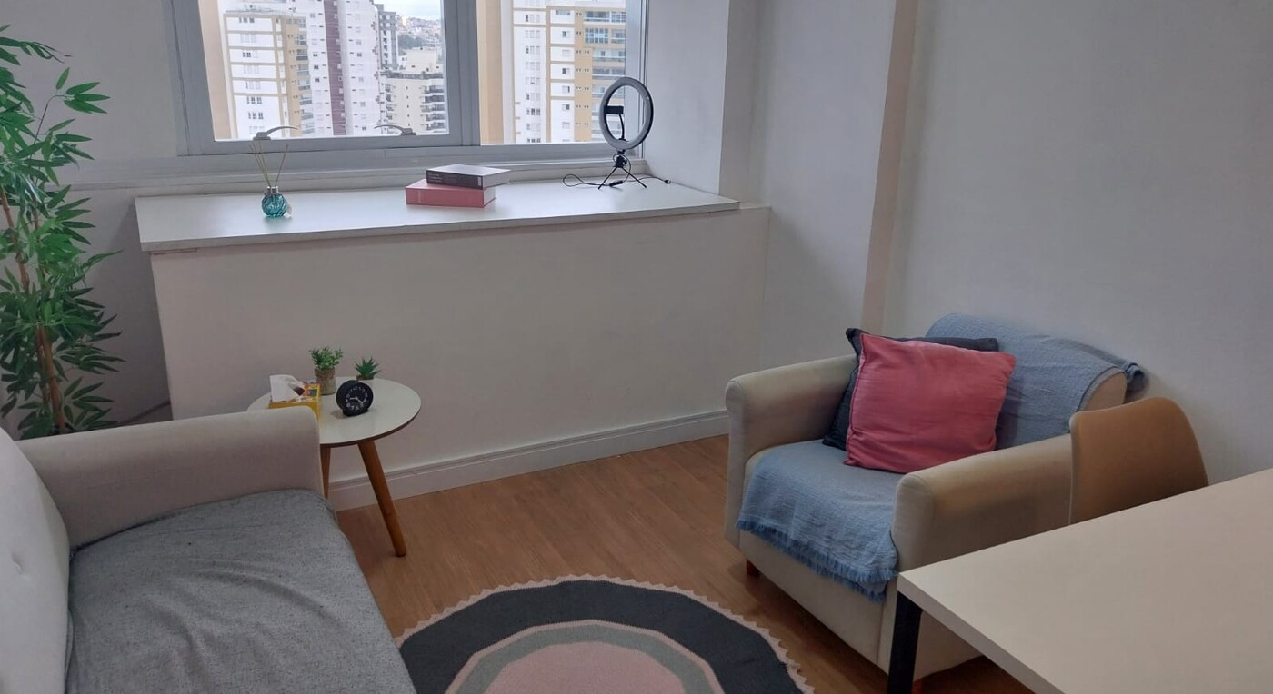 Sala de atendimento em andar alto, com poltronas, planta e janela ampla com vista para a cidade