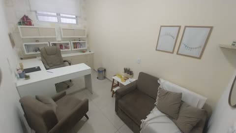 Sala de atendimento com mesa, poltrona e sofá, com cantinho lúdico para crianças